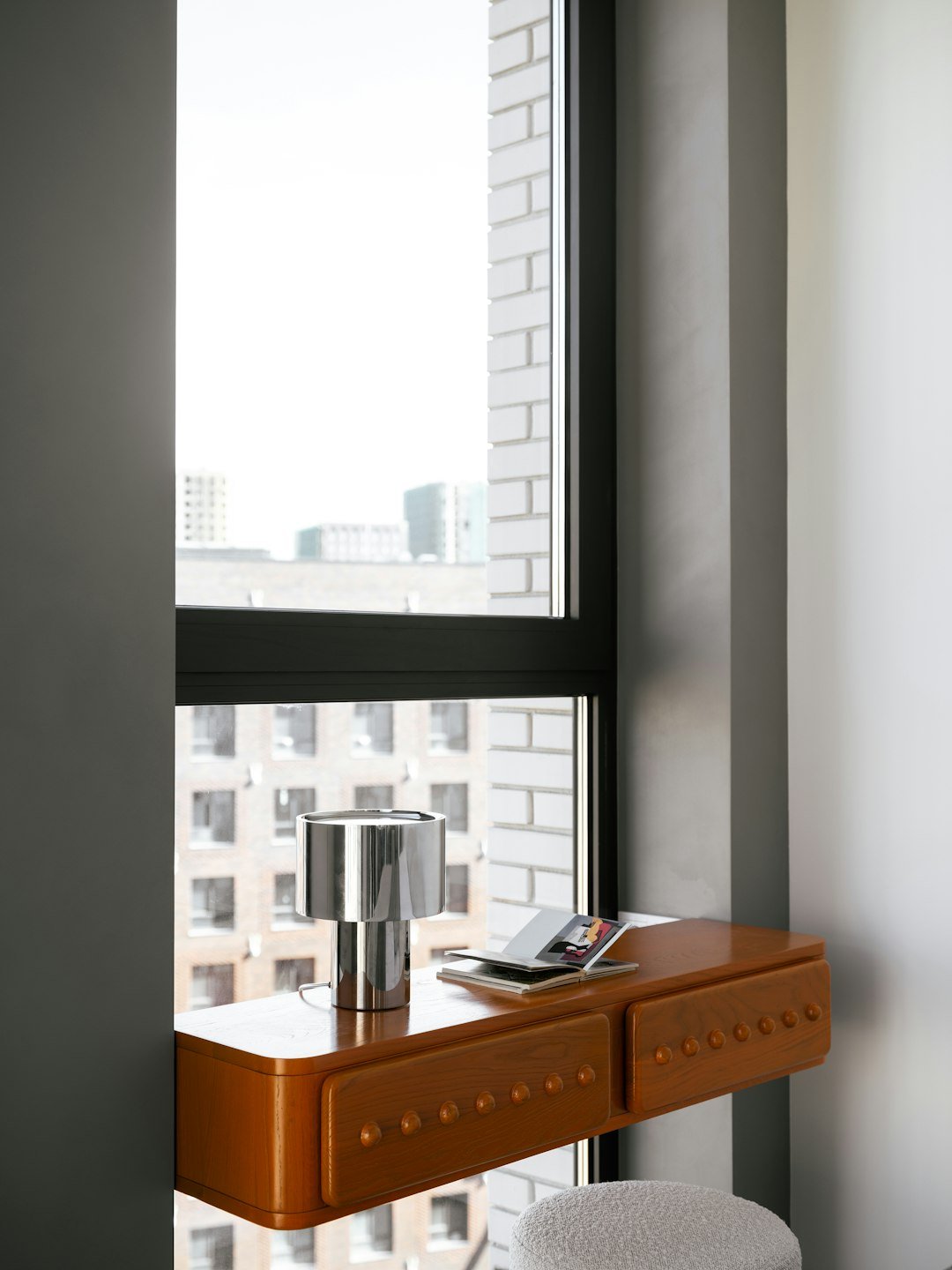 A desk with a lamp sits by a window.